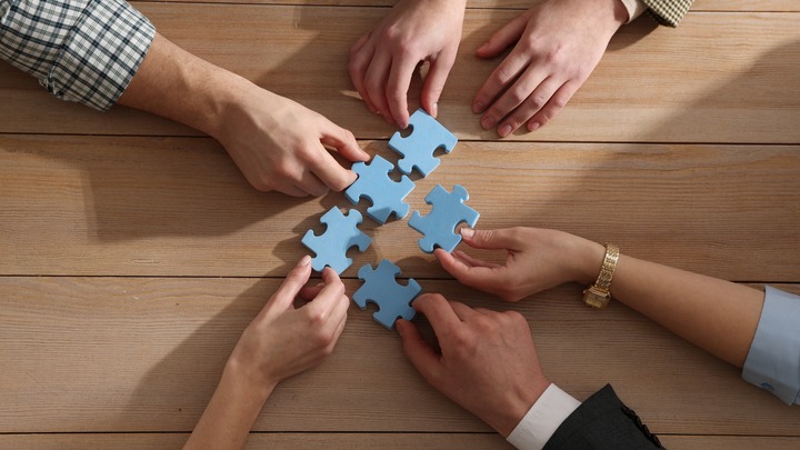 Hände halten einzelne Puzzleteile, die zusammenpassen